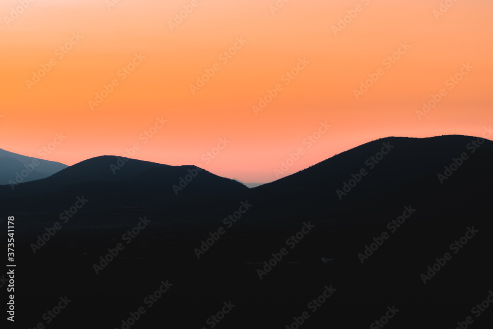 Morning sunrise landscape at the mountains in a beatiful day. Black shadowed mountains with a red and orange sunrise on background.