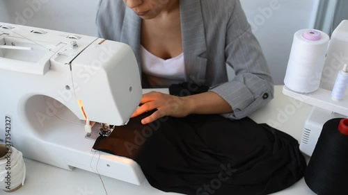 Young woman tailor is sewing on sewing machine in her mini workshop.