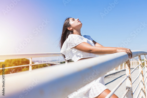 Young beautiful woman wearing hat leaning on a bridge and sunbathing © Irene