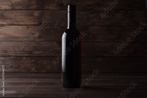A closed bottle of red wine stands on a wooden table, dark wooden boards in the background. Copy space. Winemaking presentation concept.