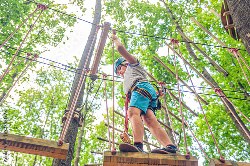 Teen boy in gear and helmet holds on to the ropes in forest adventure park