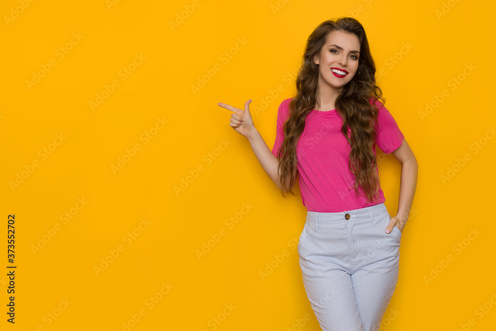 Obraz premium Casual Young Woman Is Pointing At The Side And Smiling