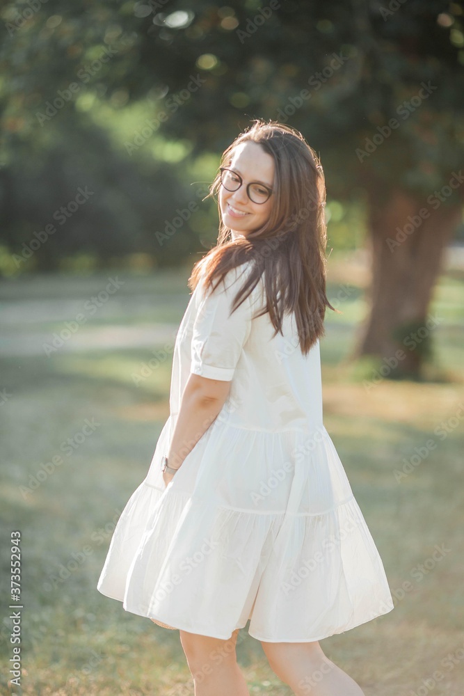 Young woman portrait in sunbeams. A beautiful young woman in a white dress with a wicker straw hat walks in the park. Summer. Young woman portrait in sunbeams. A beautiful young woman in a white dress with a wicker straw hat walks in the park. Summer.
