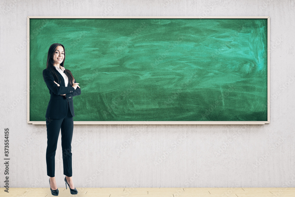 Businesswoman standing in modern classroom with empty chalkboard. Businesswoman standing in modern classroom with empty chalkboard.