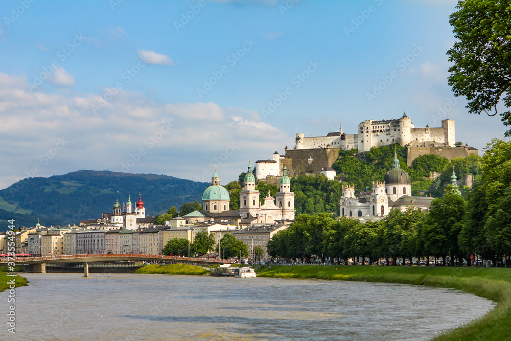 Summer landscape of a European city. Mountain river, mountains, church and fortress. Salzburg, Hohensalzburg