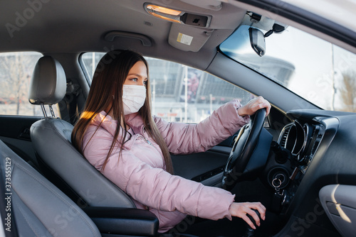 A young girl sits behind the wheel in the car in the mask during the global pandemic and coronavirus. Quarantine © Andrii