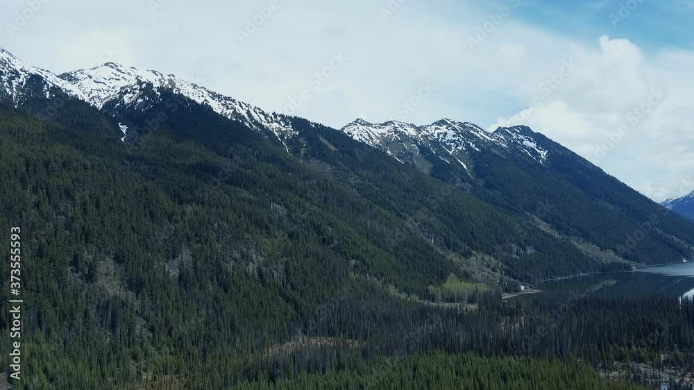 Drone view of mountains with snow peaks. Mountain hills covered with old green pine forest. Drone view of mountains with snow peaks. Mountain hills covered with old green pine forest.