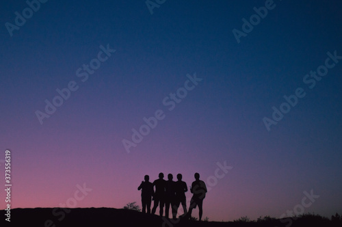 Silhouette of a group of five friends standing in front a pink sunset