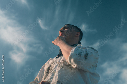 Worker dressed in dirty white clothes stands in thought on the background of blue sky photo