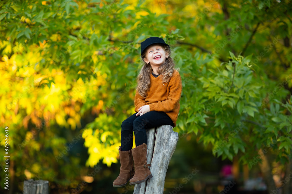 Young girl sitting up the wooden stump and smiling. Autumn background. Copy space. Young girl sitting up the wooden stump and smiling. Autumn background. Copy space.