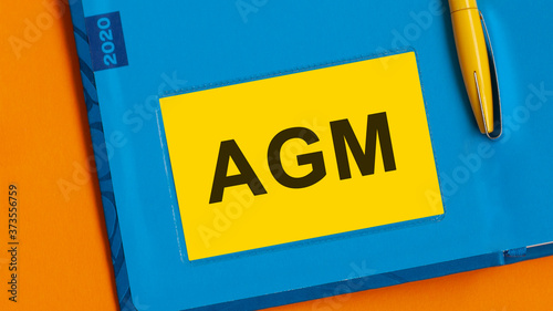 The word AGM is written in black marker on the yellow paper for notes. AGM - Annual general meeting