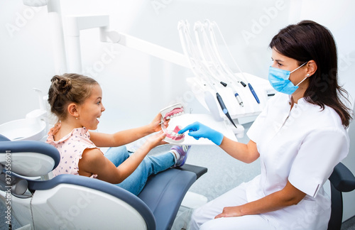 Cute little girl sitting on a dental chair having fun with a positive dentist. Kid teeth treatment