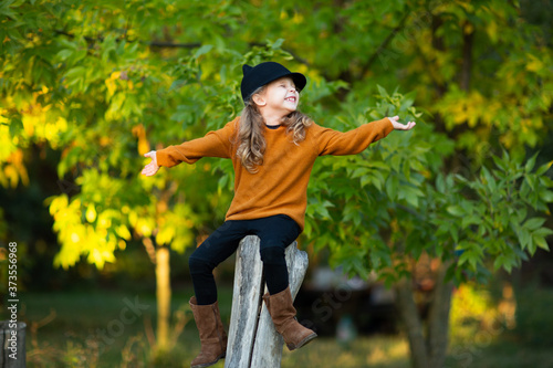 Young girl sitting up the wooden stump and smiling. Autumn background. Copy space.