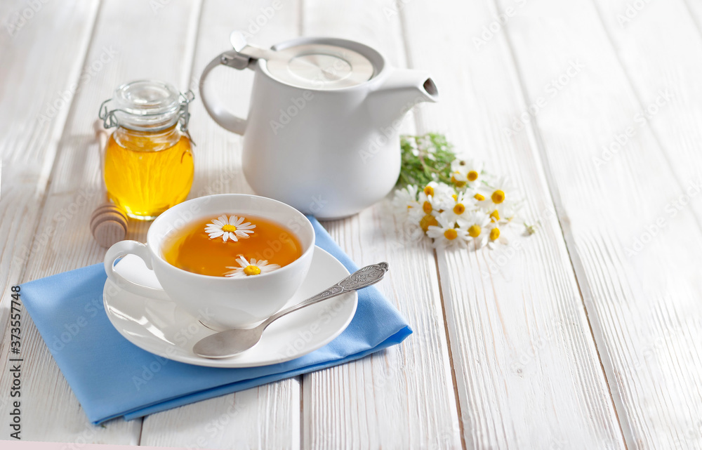 Cup of herbal tea with honey and chamomile flowers on the white wooden background. Natural alternative medicine Cup of herbal tea with honey and chamomile flowers on the white wooden background. Natural alternative medicine