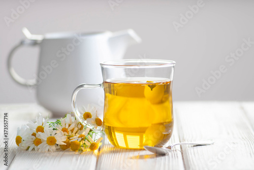 Cup of herbal tea with chamomile flowers on the white wooden background. Natural organic alternative medicine concept