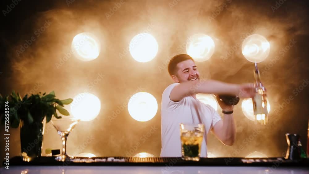 Attractive bartender professionally juggling cups and doing a show in beautiful modern bar. Slow motion