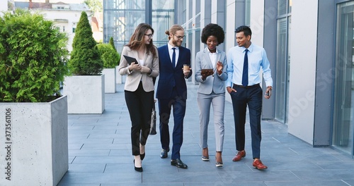 Obraz na plátně Mixed-races young cheerful people in business style walking the street , laughing and talking