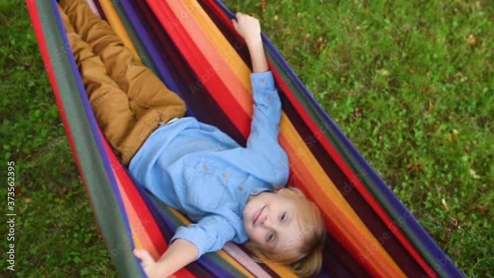 Cute little boy having fun on outdoor playground.Child loves playing or just lying in hammock.Summer leisure for kids. How to entertain child in yard in summer.Activities and fun for children outdoors Cute little boy having fun on outdoor playground.Child loves playing or just lying in hammock.Summer leisure for kids. How to entertain child in yard in summer.Activities and fun for children outdoors