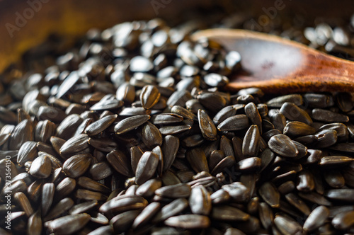 Fried sunflower black seeds with a wooden spoon in a pan, close-up