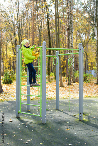 Fototapeta Naklejka Na Ścianę i Meble -  Beautiful teenager daughter in an green jacket plaing on the playground in the autumn park. Horizontal photo