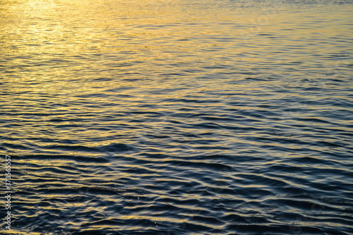 Reflection of the sun on golden hour on calm ocean water texture. Calm sea at sunset.