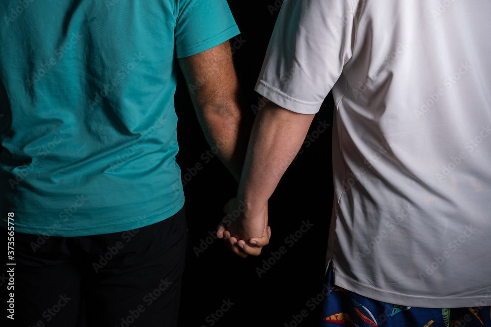 Fototapeta premium Gay interracial young couple holding hands in black background
