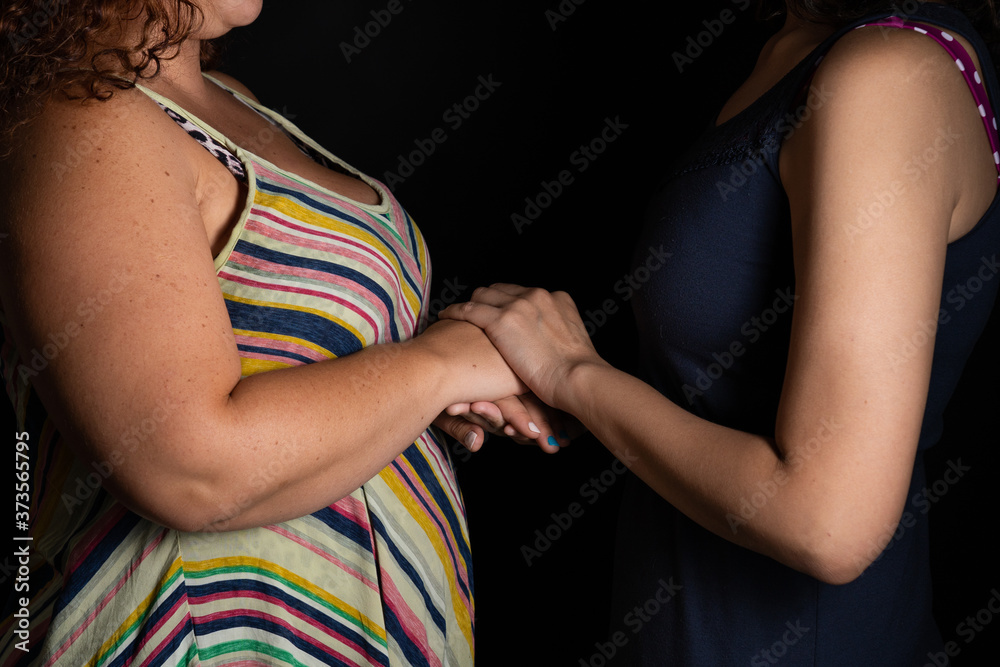 Lesbian young couple holding hands wearing dresses in black background