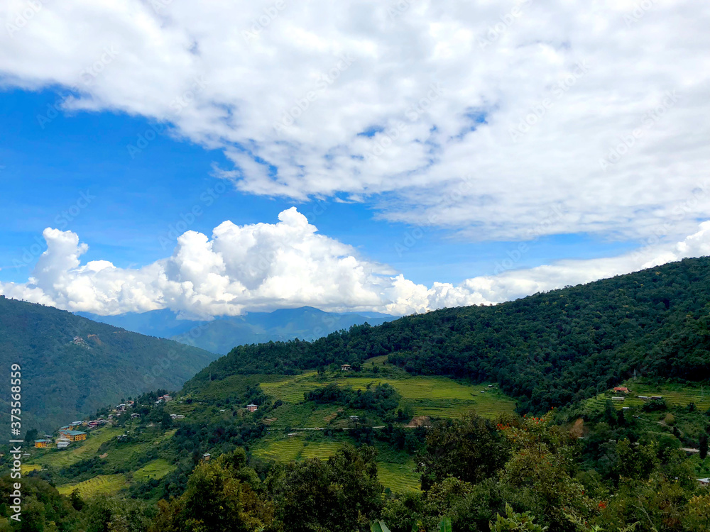 Bhutanese Countryside with Rice Paddies, Mountains, and Clouds in View