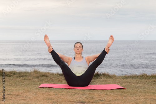 Woman doing pilates outdoors with the sea in the background.