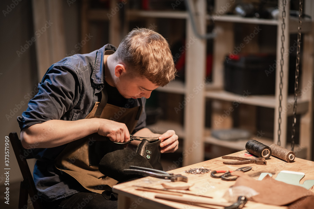 a young man is engaged in the family craft of making leather shoes in a workshop a young man is engaged in the family craft of making leather shoes in a workshop