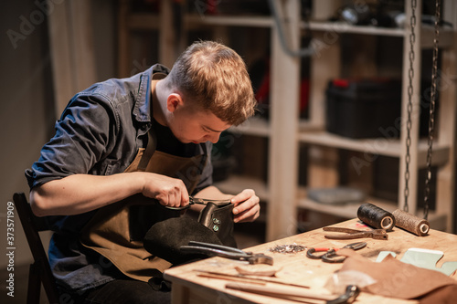 a young man is engaged in the family craft of making leather shoes in a workshop photo