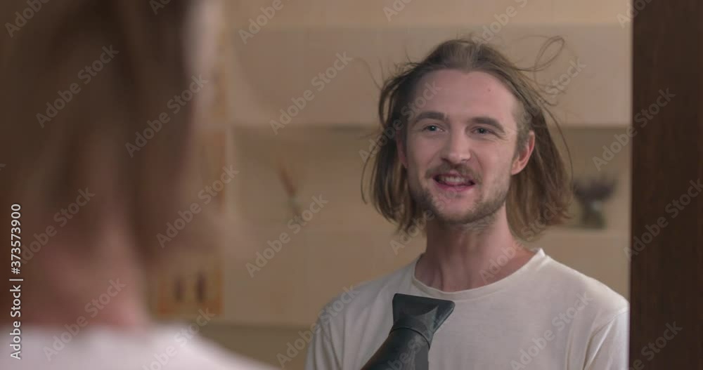 Young man looks at mirror, dries his hair, sings in hairdryer as a microphone Young man looks at mirror, dries his hair, sings in hairdryer as a microphone
