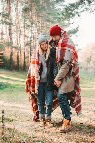 Couple huggings travelers covered with plaid in the forest. Concept of trekking, adventure and seasonal vacation.