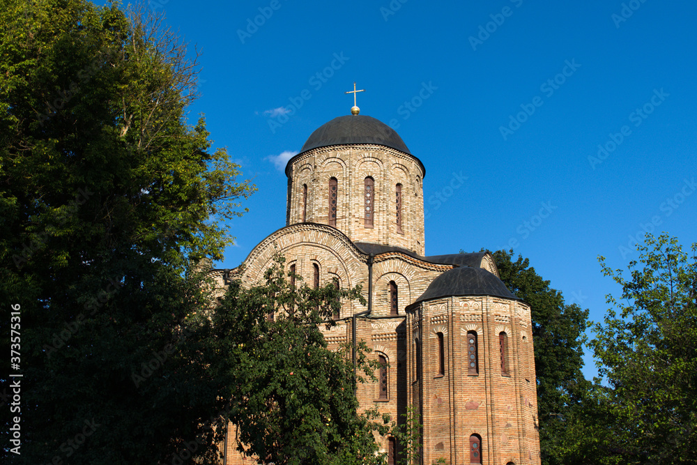 ancient temple with cross on central tower on blue sky background and dark greenery of garden