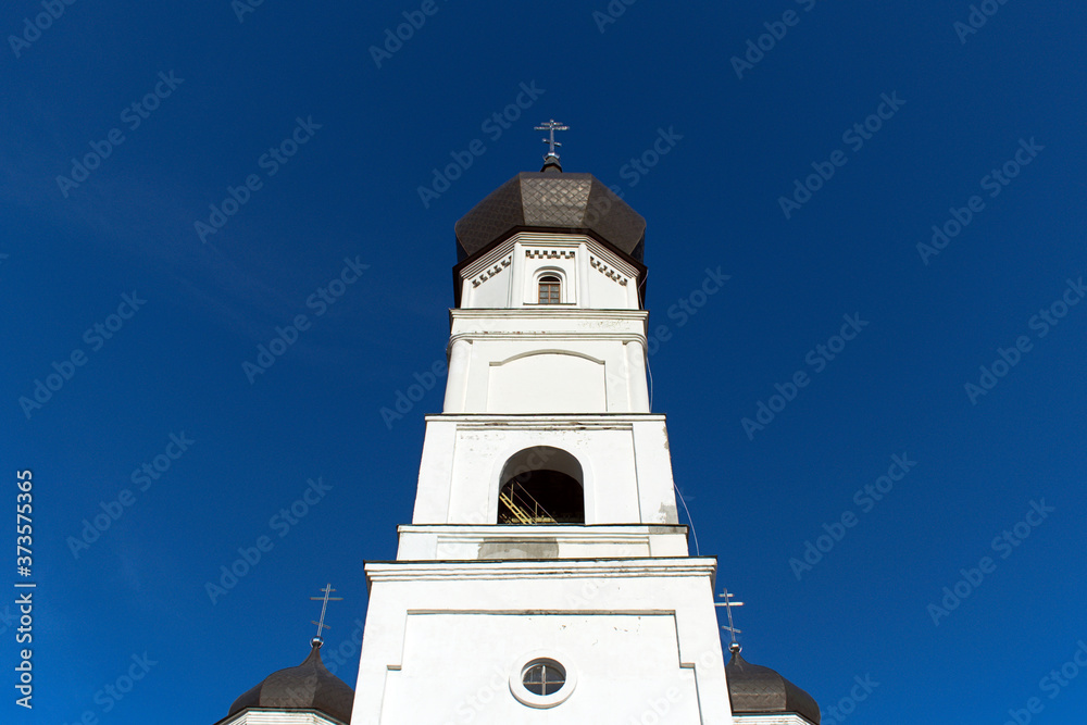 bright white central tower of orthodox cathedral with cross on blue sky background