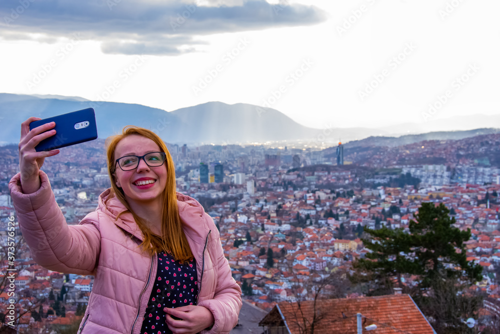 girl with glasess and brown hair taking selfie above Sarajevo capital of BiH with mobile phone