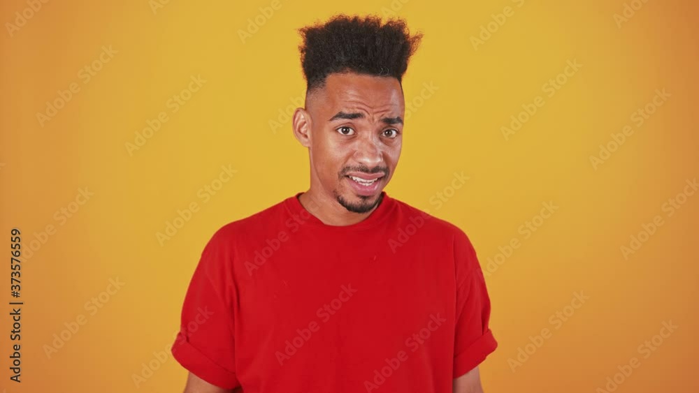 Close up portrait of young black guy trying to hear you, putting hand to ear, orange studio background Close up portrait of young black guy trying to hear you, putting hand to ear, orange studio background