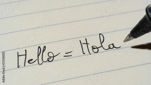 Beginner Spanish language learner writing Hello word Hola for homework on a notebook photo