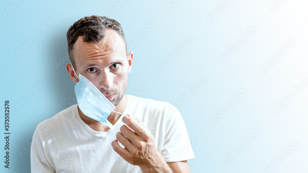 young man putting on a medical mask on his face on blue background with copy space young man putting on a medical mask on his face on blue background with copy space