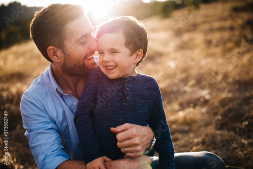 father holding son smiling in a field with golden light