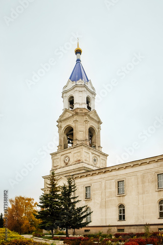 Ancient christian church and autumn yellow trees. Beautiful domes, high old bell tower against the sky