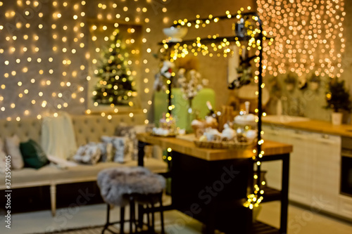 Blurred Christmas background with Christmas tree and lights. A lot of glare and blurred bokeh Golden brown. Kitchen in Christmas lights garlands.