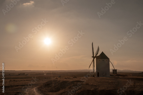 Un molino de viento tradicional del siglo XVI mira al sol mientras este se pone por el Oeste. Castilla La Mancha.