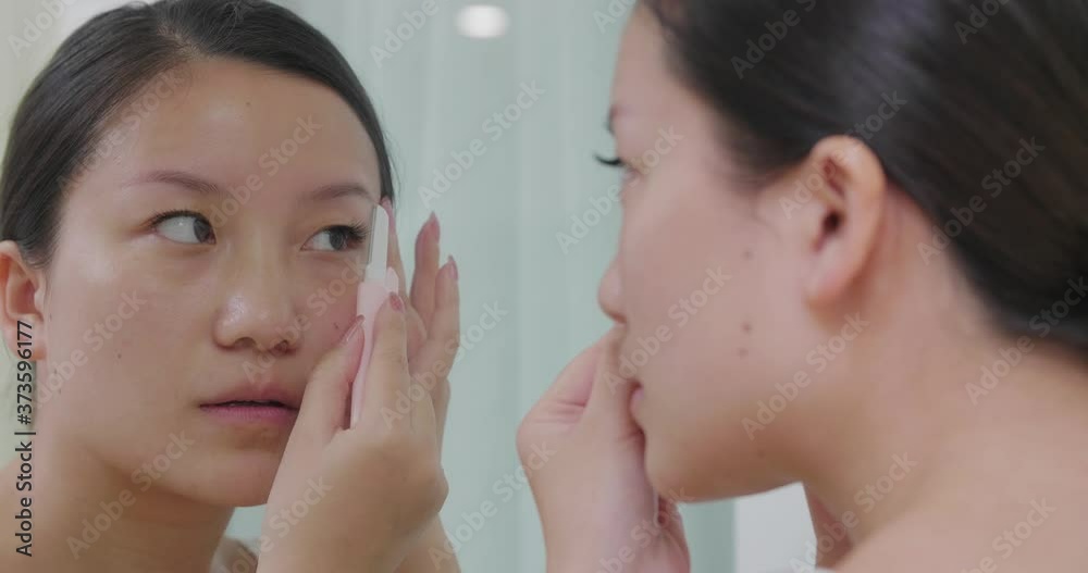Close up of one pretty young Chinese woman face the mirror make up in the morning examining her face taking care of her eyebrow 