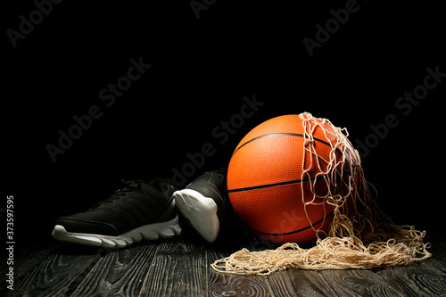 Ball for playing basketball, shoes and net on table against dark background © Pixel-Shot