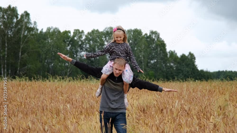 Dad Giving Daughter Piggyback Ride in a Wheat Field. Child Flying on Father Shoulders. Slow Motion. Concept of Fathers Day, Freedom, Harmony with Nature and Summer Vacation Dad Giving Daughter Piggyback Ride in a Wheat Field. Child Flying on Father Shoulders. Slow Motion. Concept of Fathers Day, Freedom, Harmony with Nature and Summer Vacation