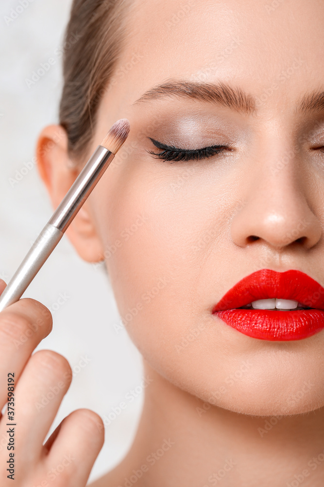 Makeup artist working with model on light background, closeup