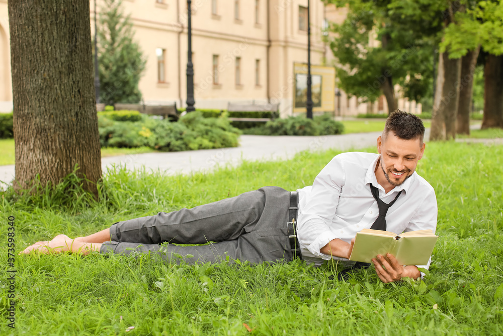Handsome businessman reading book while relaxing in park Handsome businessman reading book while relaxing in park