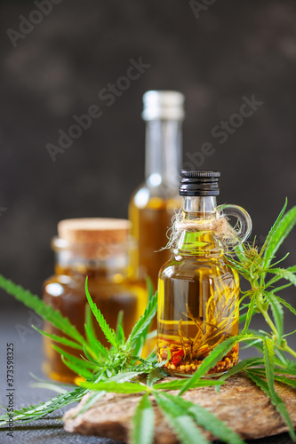 Oil in bottle and leaves of hemp on a stone podium on dark background.