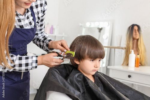 Female hairdresser working with little boy in salon